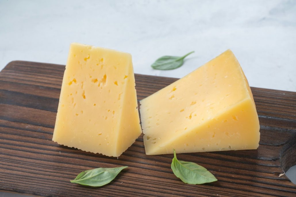 Two triangular blocks of hard cheese and three basil leaves